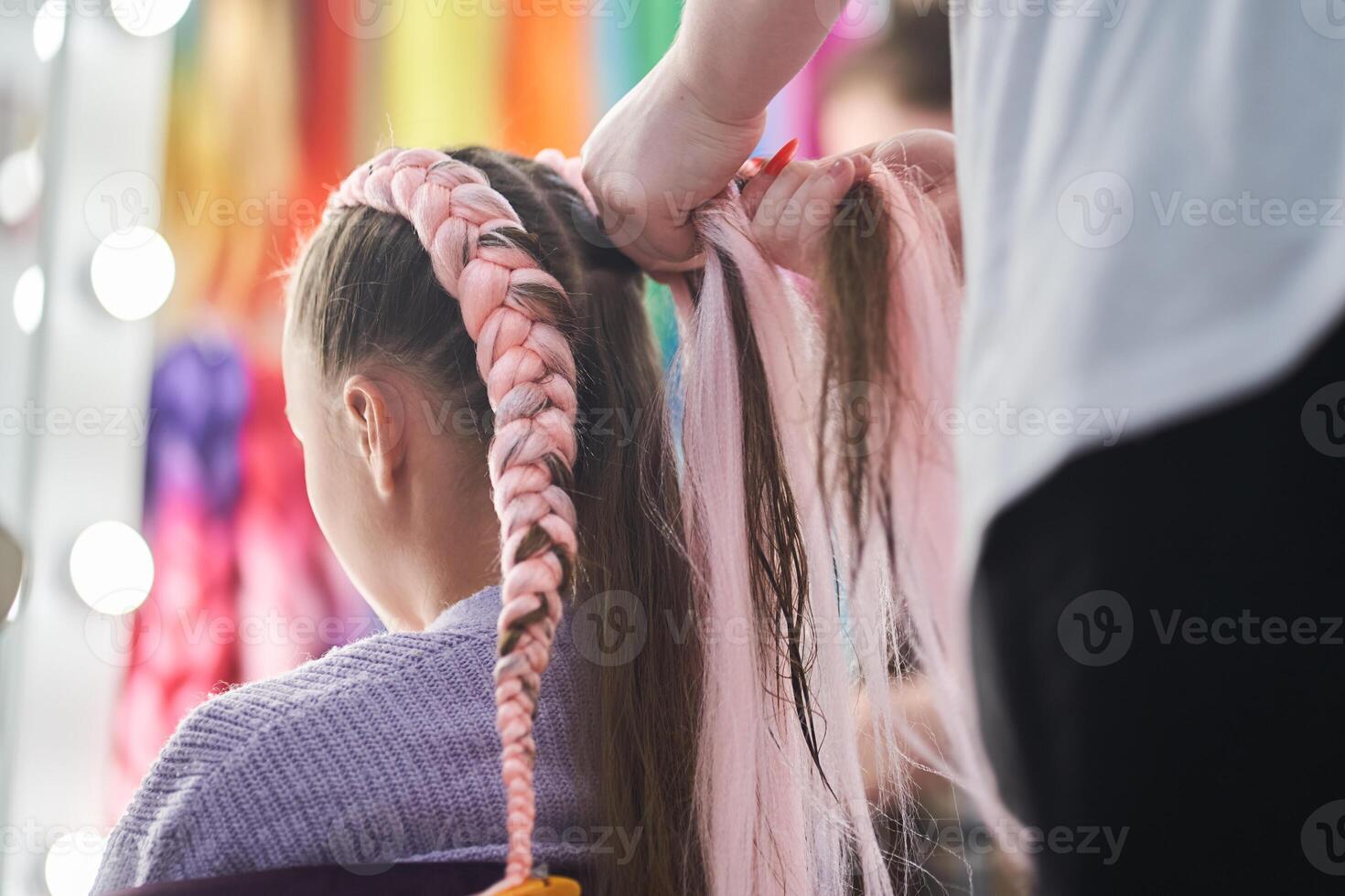 The hands of the master who weave the kanekalon material into the hair. The master braids the child's pigtails from a pink kanekalon. Rear view with copy space photo