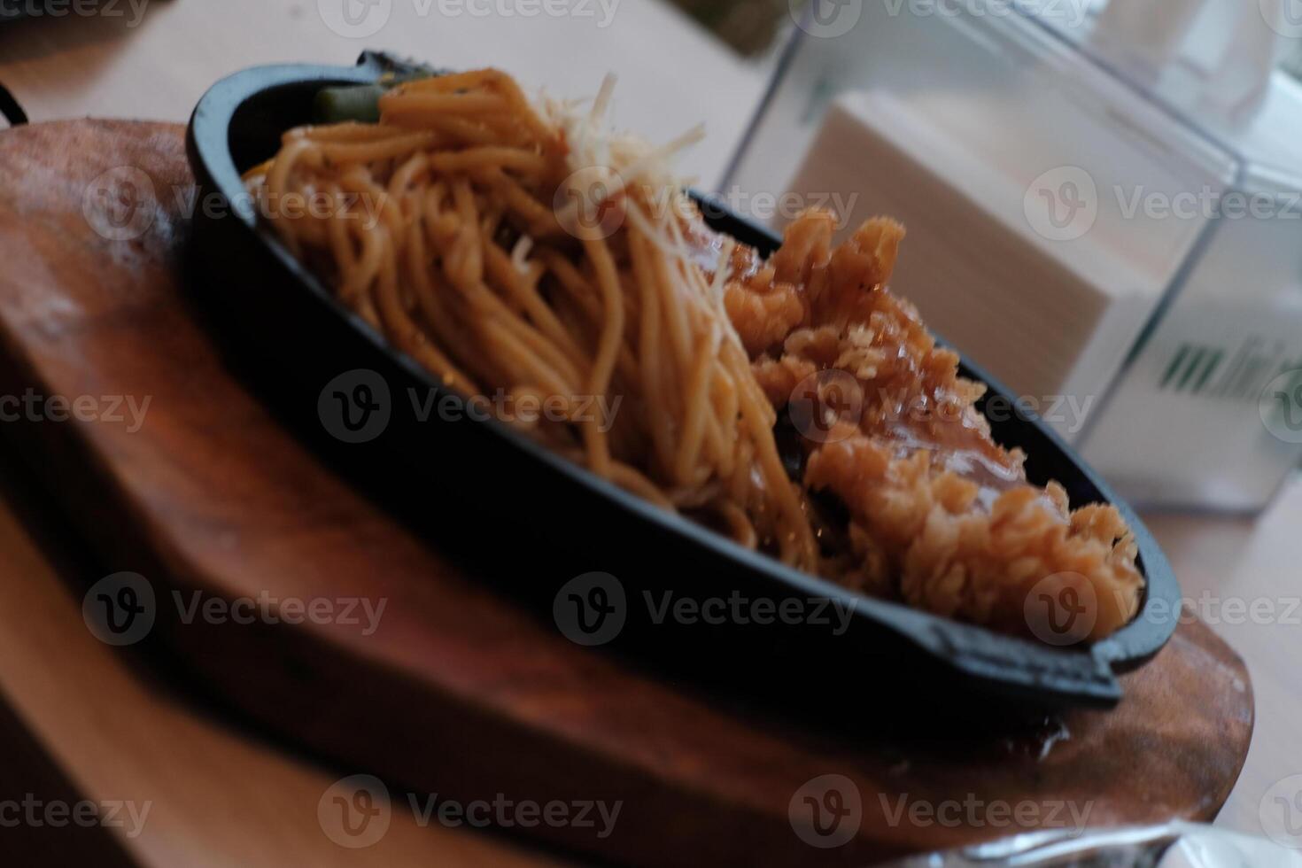 A delicious combination of crispy chicken and flavorful noodles served on a hot plate with vegetables. photo