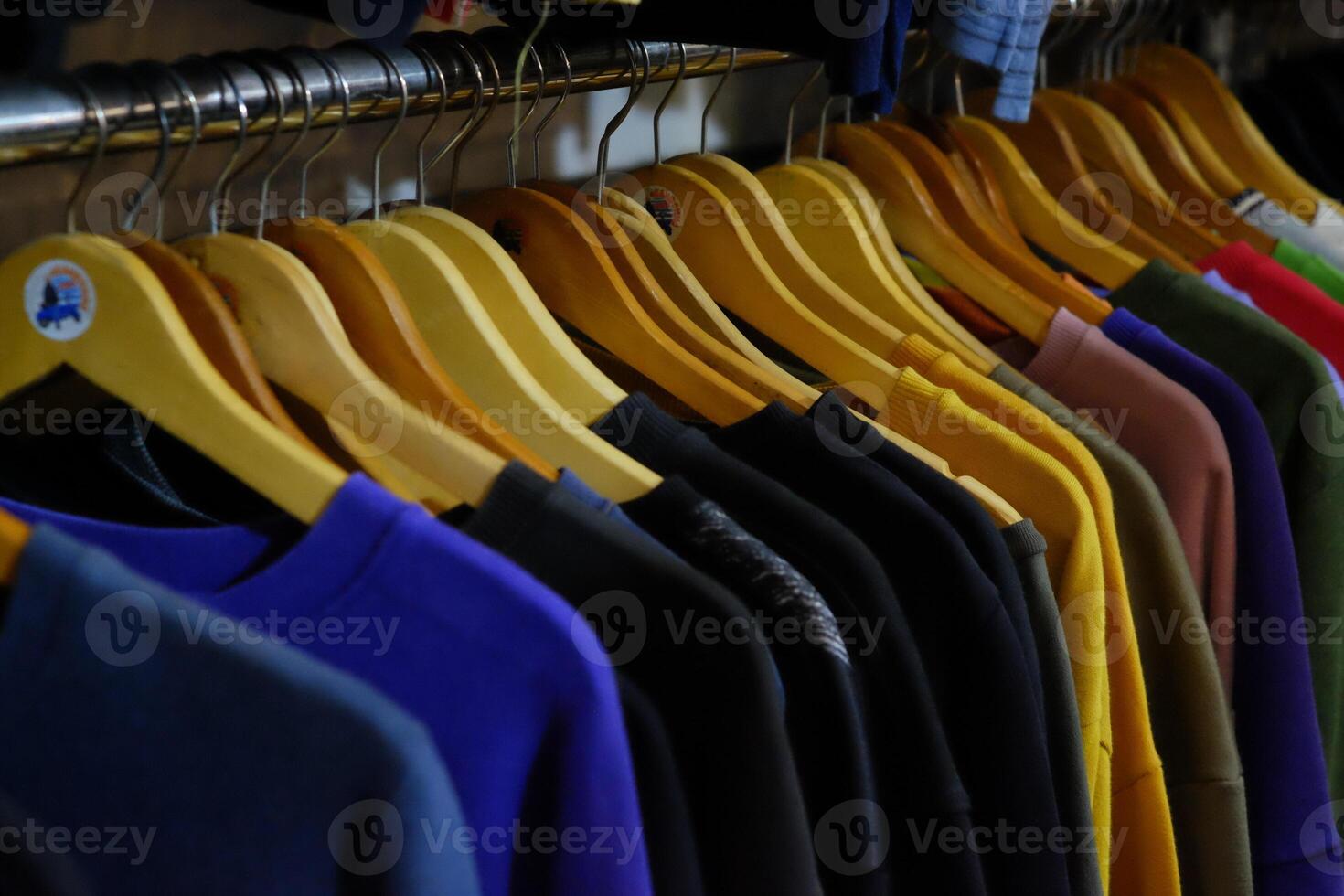 Thrifting's vibrant collection of sweaters, shirts, hoodies, trousers and knitted t-shirts are elegantly displayed on wooden hangers, featuring a variety of colors and textures. photo