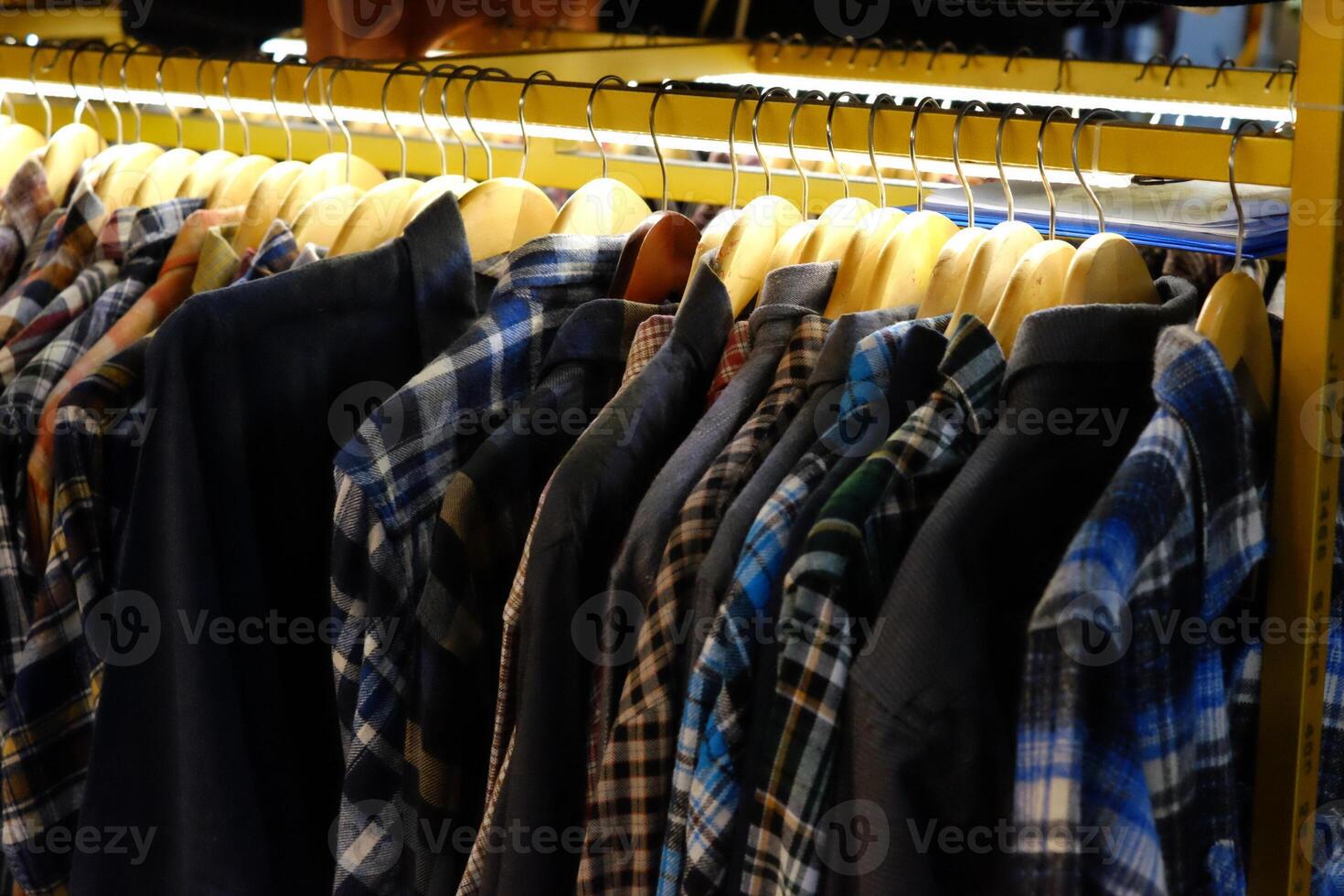 Thrifting's vibrant collection of sweaters, shirts, hoodies, trousers and knitted t-shirts are elegantly displayed on wooden hangers, featuring a variety of colors and textures. photo