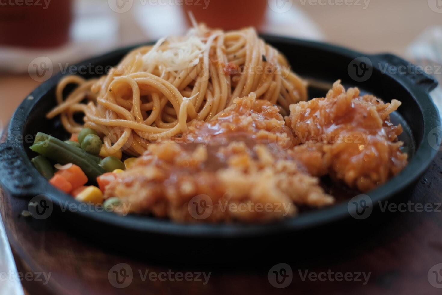 A delicious combination of crispy chicken and flavorful noodles served on a hot plate with vegetables. photo