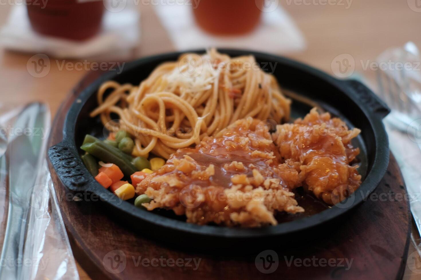 A delicious combination of crispy chicken and flavorful noodles served on a hot plate with vegetables. photo