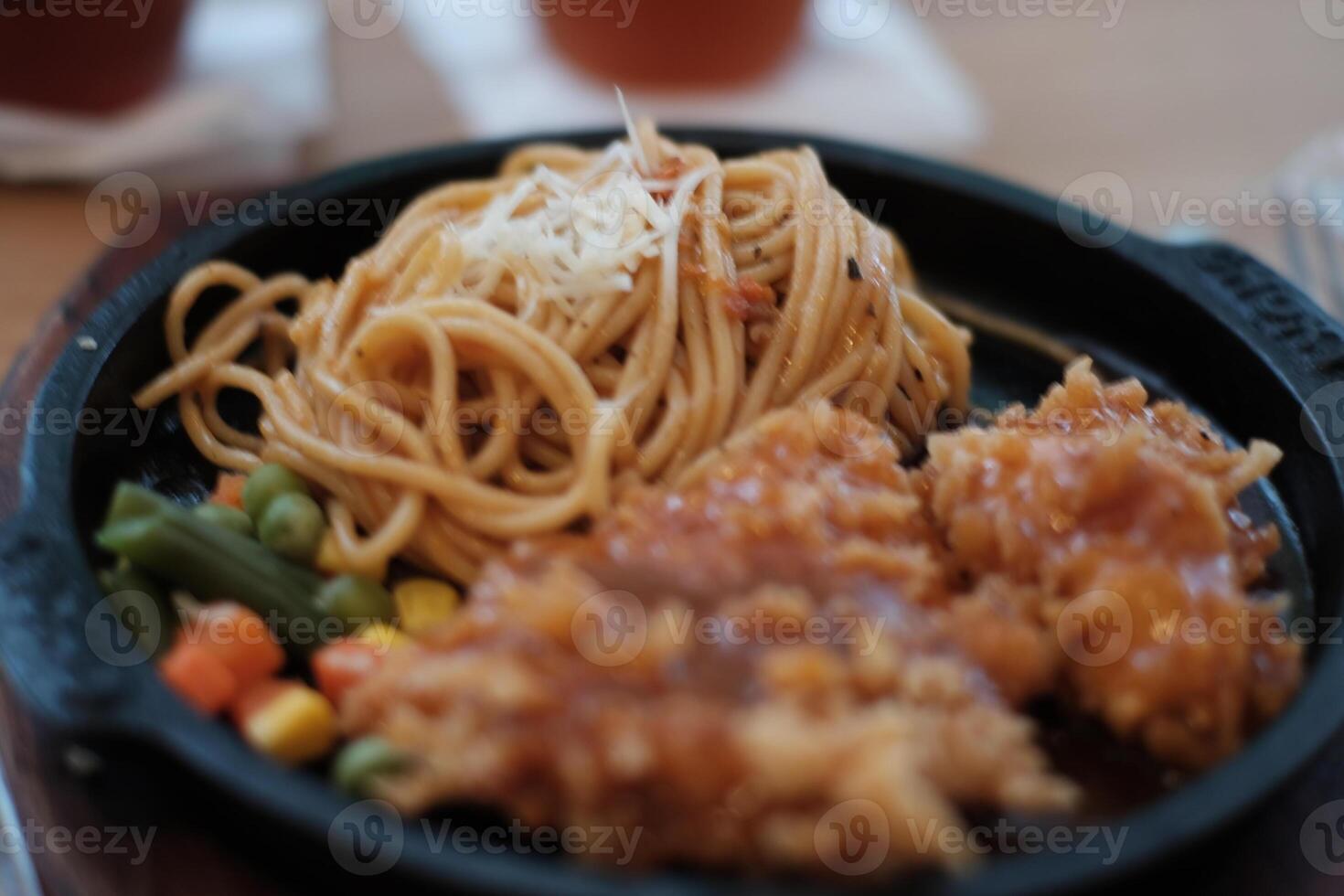 A delicious combination of crispy chicken and flavorful noodles served on a hot plate with vegetables. photo