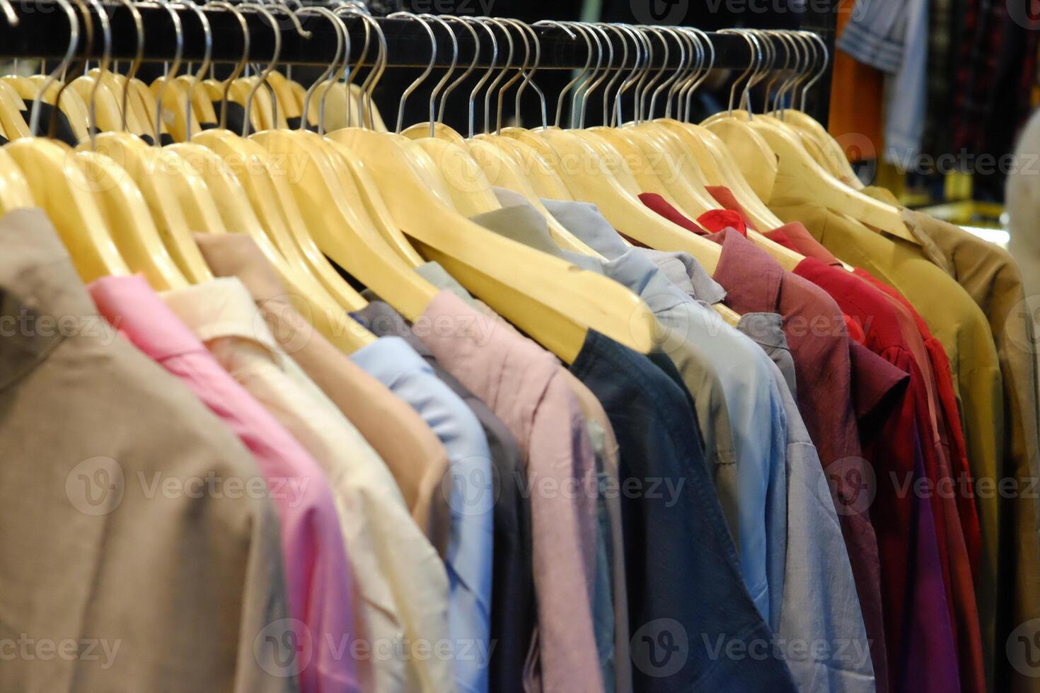 Thrifting's vibrant collection of sweaters, shirts, hoodies, trousers and knitted t-shirts are elegantly displayed on wooden hangers, featuring a variety of colors and textures. photo