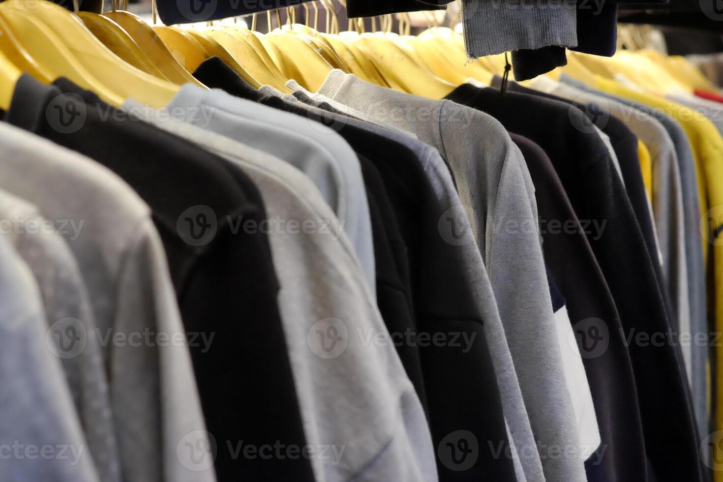 Thrifting's vibrant collection of sweaters, shirts, hoodies, trousers and knitted t-shirts are elegantly displayed on wooden hangers, featuring a variety of colors and textures. photo
