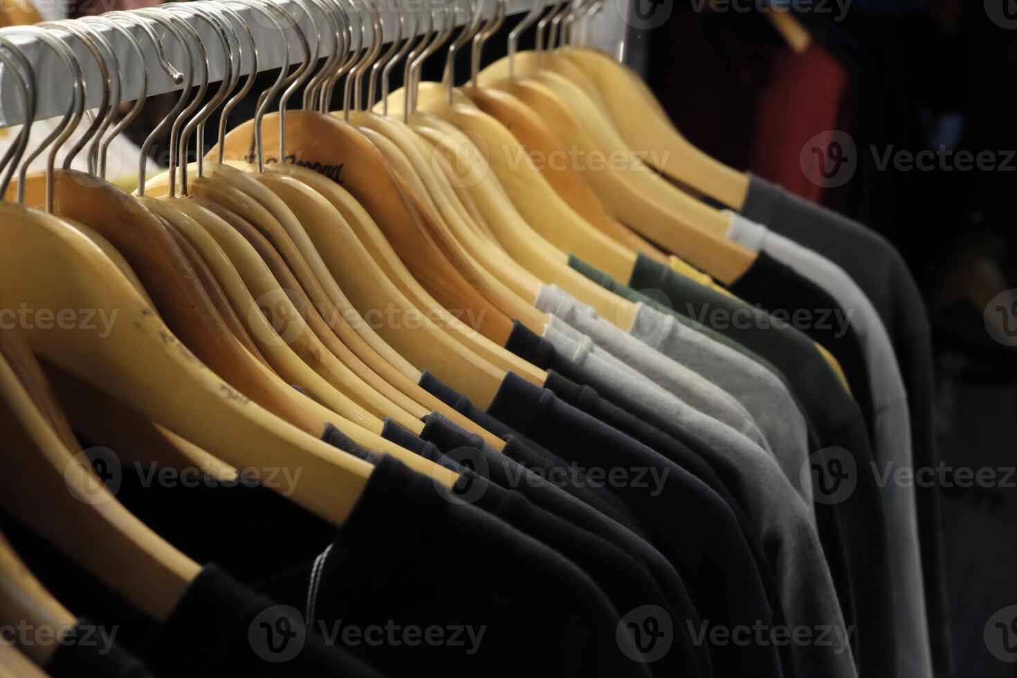 Thrifting's vibrant collection of sweaters, shirts, hoodies, trousers and knitted t-shirts are elegantly displayed on wooden hangers, featuring a variety of colors and textures. photo