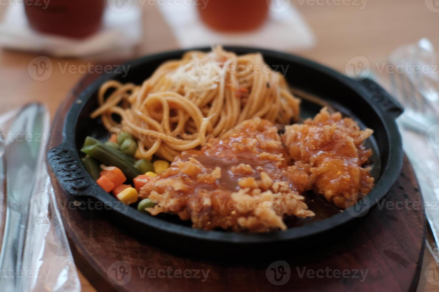 A delicious combination of crispy chicken and flavorful noodles served on a hot plate with vegetables. photo