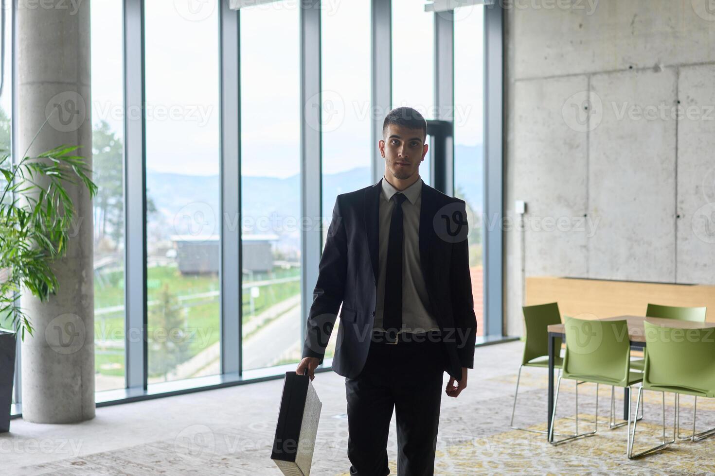 A determined businessman in a black suit confidently walks through the office, embodying professionalism and focus as he heads towards new challenges photo