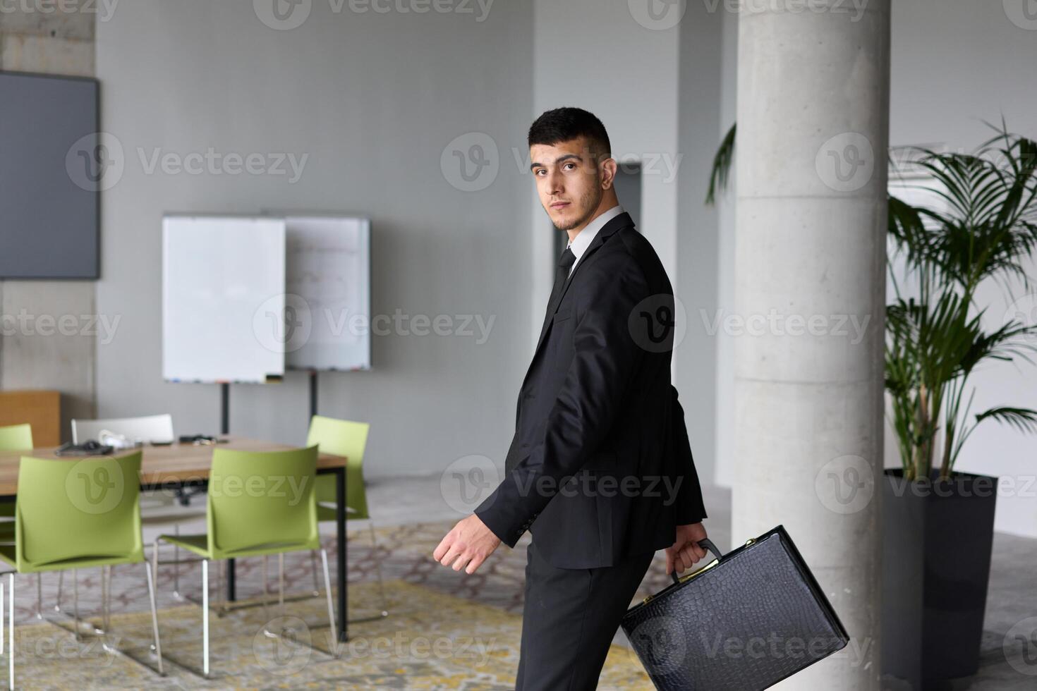 A determined businessman in a black suit confidently walks through the office, embodying professionalism and focus as he heads towards new challenges photo