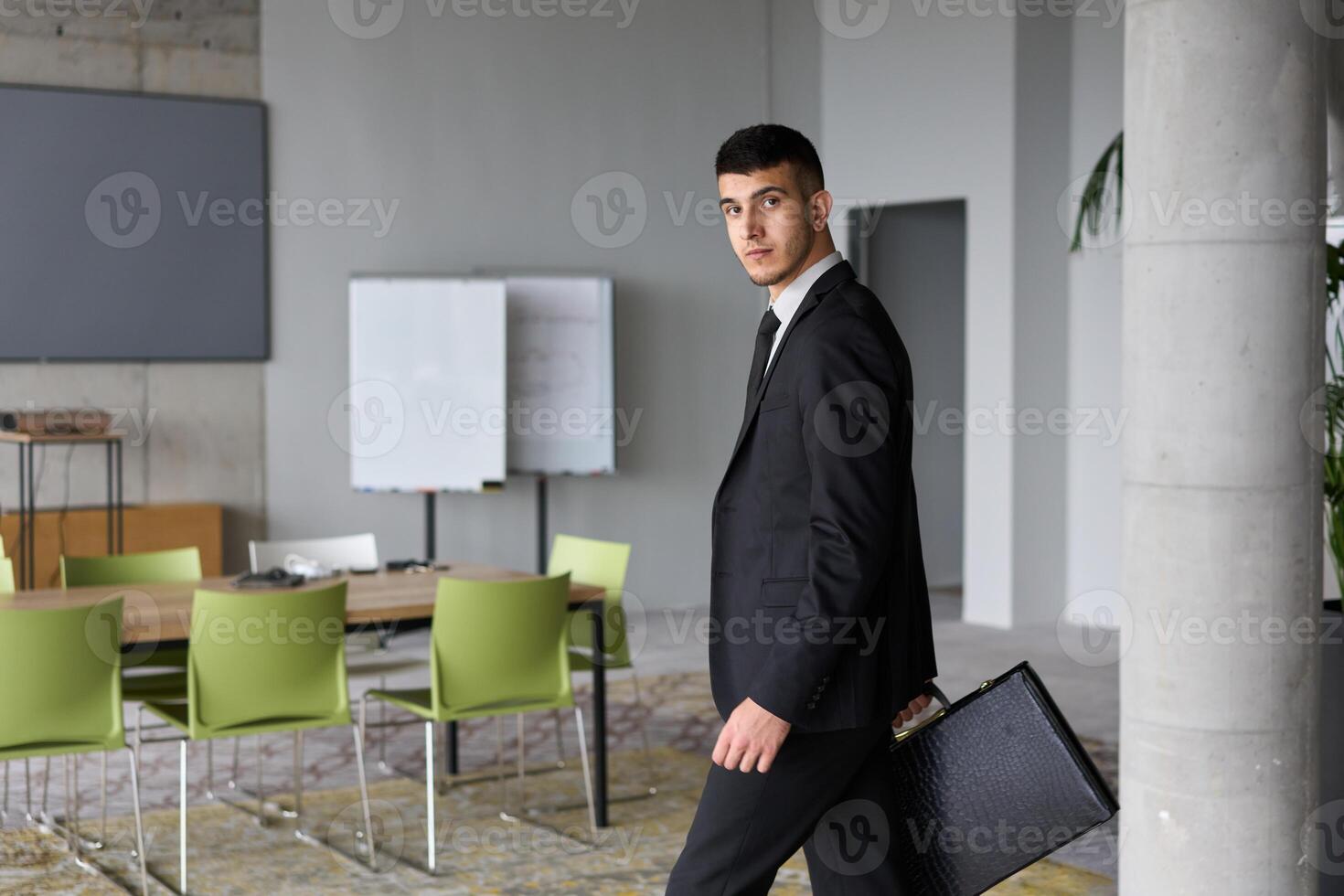A determined businessman in a black suit confidently walks through the office, embodying professionalism and focus as he heads towards new challenges photo