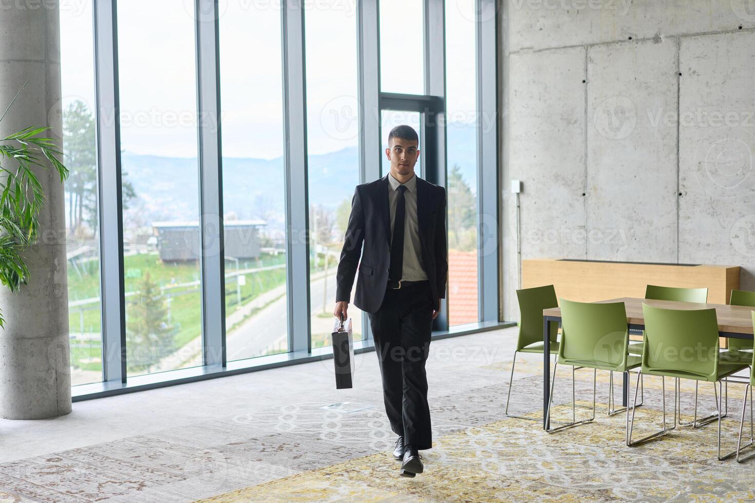 A determined businessman in a black suit confidently walks through the office, embodying professionalism and focus as he heads towards new challenges photo