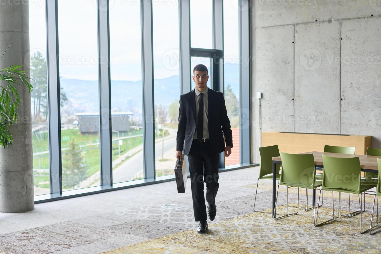 A determined businessman in a black suit confidently walks through the office, embodying professionalism and focus as he heads towards new challenges photo