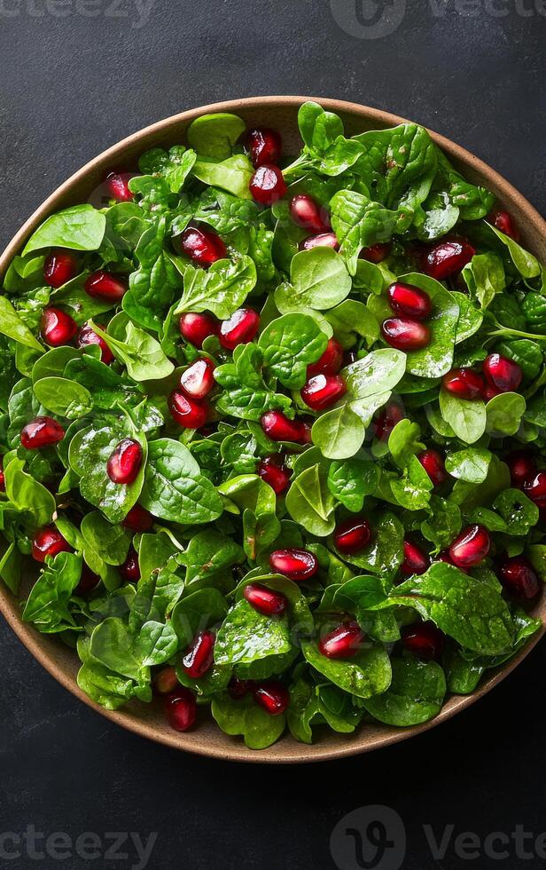 A bowl of salad with green spinach and red pomegranates. The salad is served in a brown bowl photo