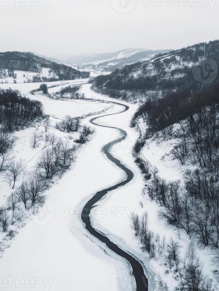 Serene Aerial View of a Winding River Surrounded by Snow-Covered Hills and Leafless Trees in a Captivating Winter Landscape photo