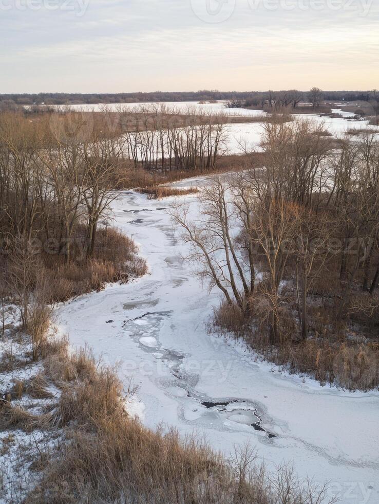 Scenic Winter Landscape with Frozen River, Bare Trees, and Calm Waters from Above, Showcasing Nature's Serene Beauty in a Cold Environment at Dusk photo