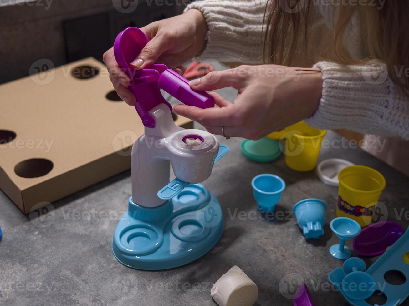 Young woman using modeling clay extruder toy set, feeding clay into machine to craft different shapes, fostering creativity and improving fine motor skills Young woman helps children photo