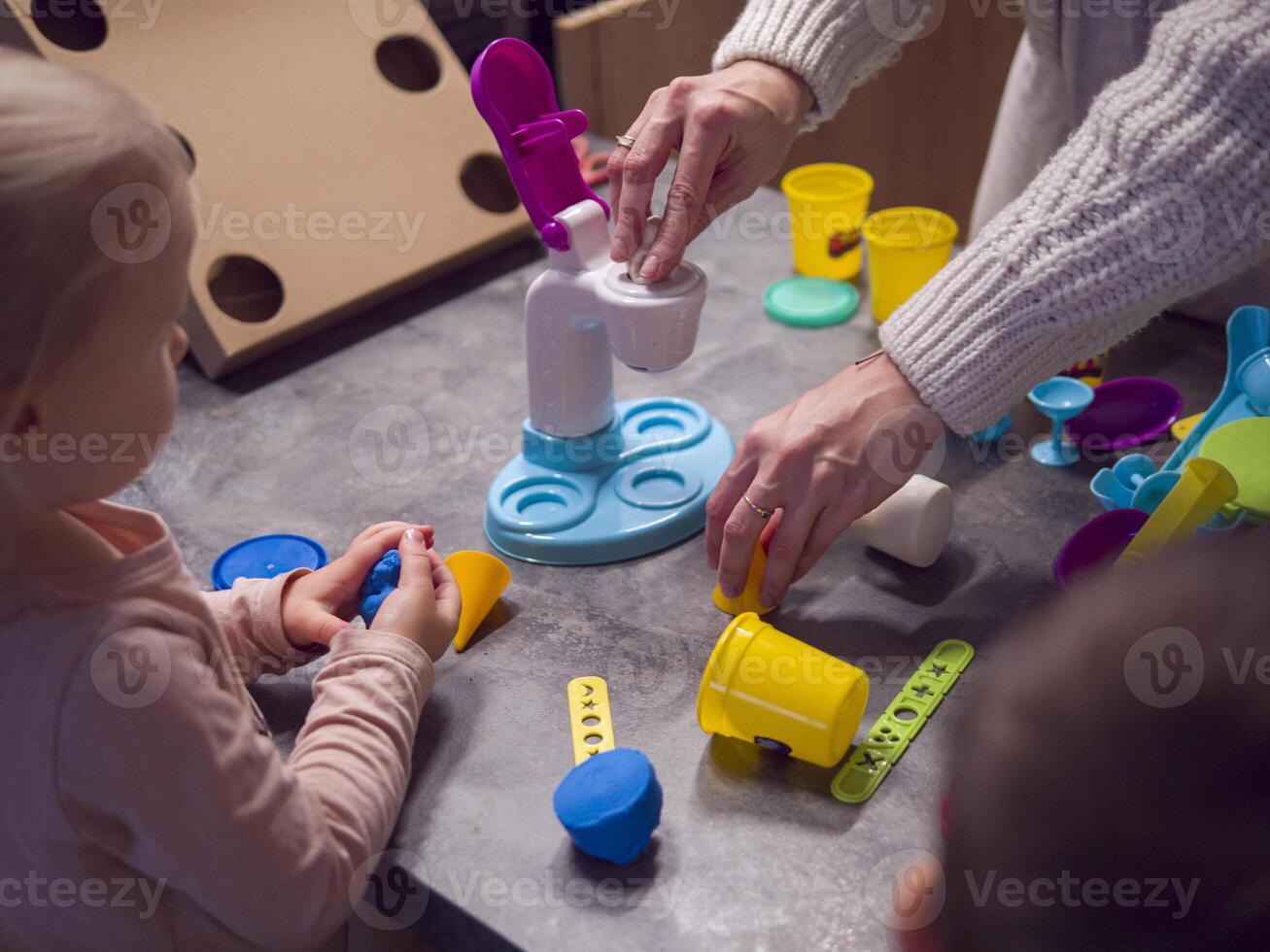 Mother and children enjoy creative playtime, shaping colorful modeling clay with tools and molds. Using tools enhances their creativity and brings fun to crafting vibrant shapes on the kitchen table. photo