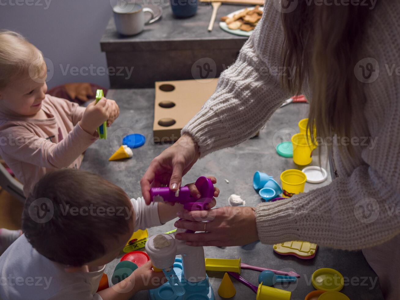 .Mother and her two children enjoy quality time together, engaging in creative play with colorful modeling clay at their kitchen table. Modeling clay and fun tools Hand Motor Concept photo