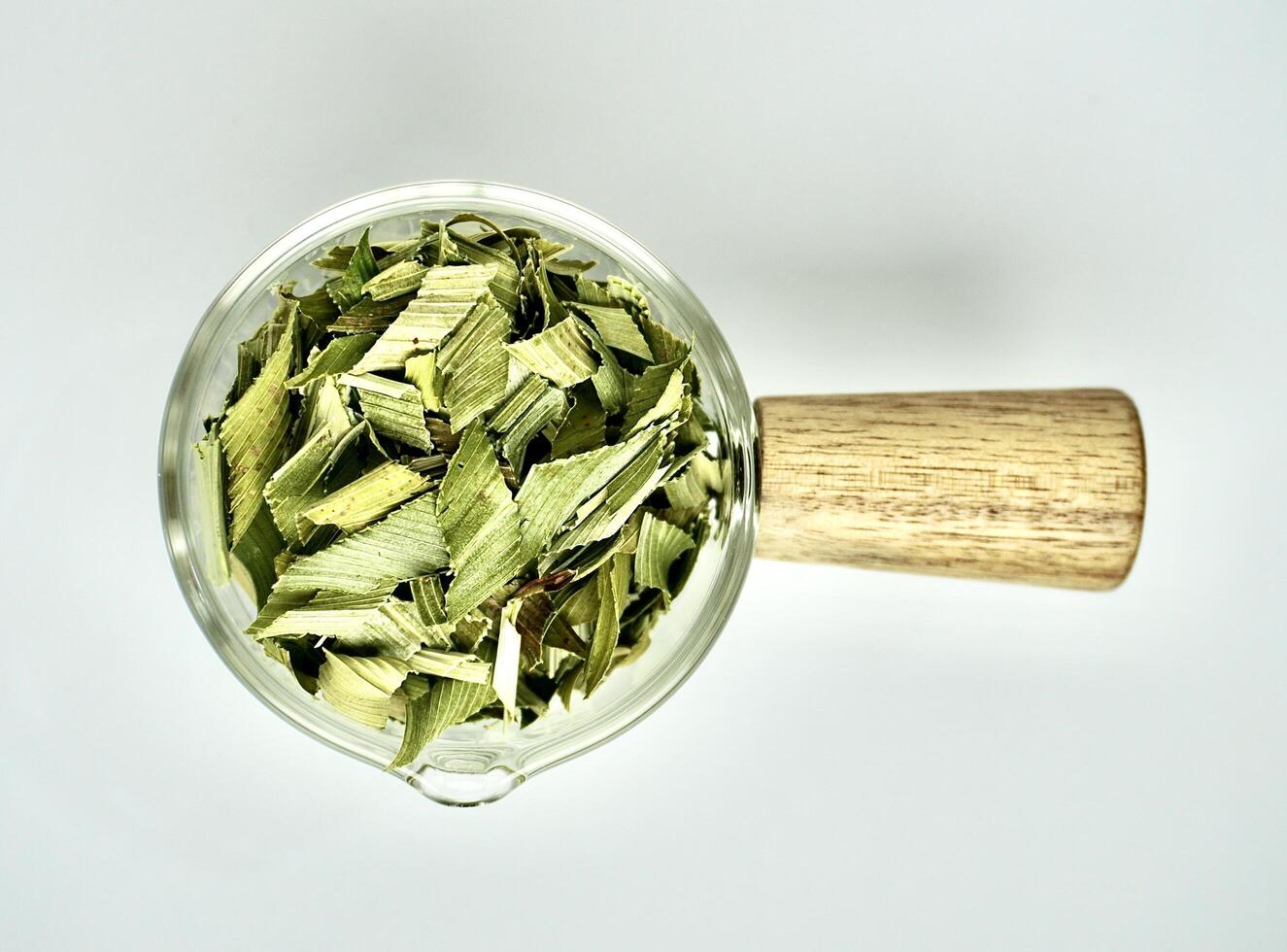 Group of dried green sliced pandan herb organic leaves in glass cup with wooden handle isolated on horizontal white background from top angle view. photo