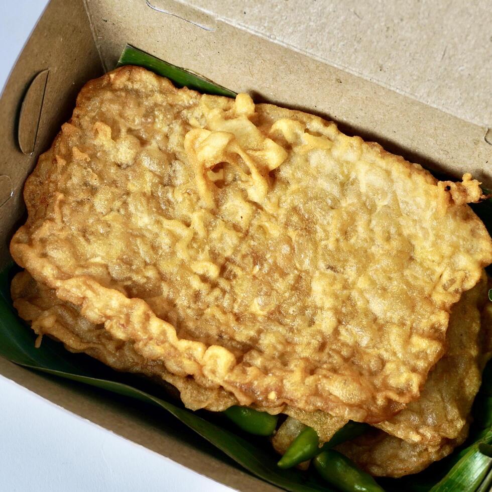 Yummy fried tempeh or tempe goreng crispy savory snack isolated on take away paper bowl box background. photo