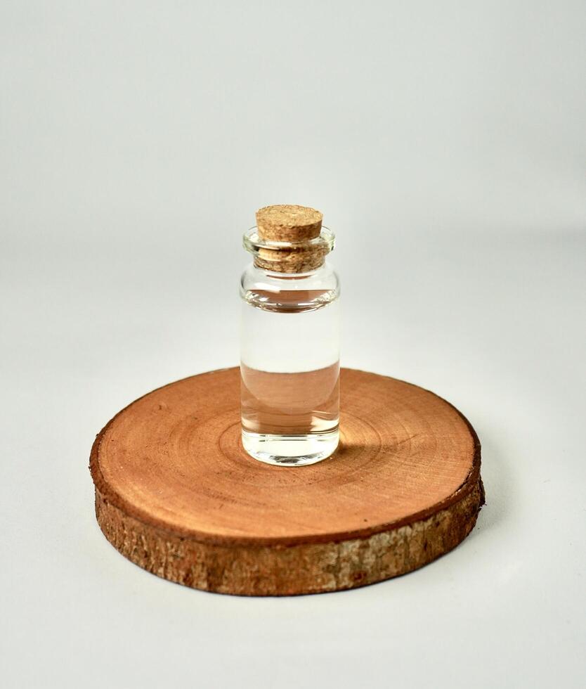 Transparent glass vial bottle container with brown cork stopper lid on wooden coaster isolated on vertical white background. photo