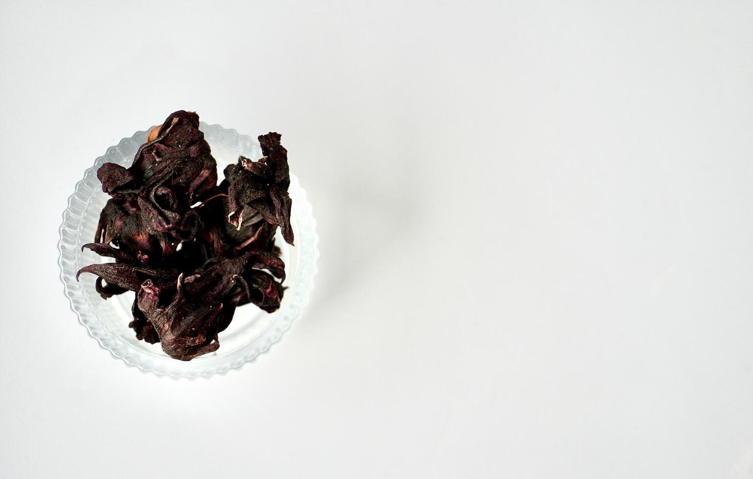 Dry purple rosella hibiscus flower herb tea in round glass bowl isolated on horizontal copy spaced white background. photo