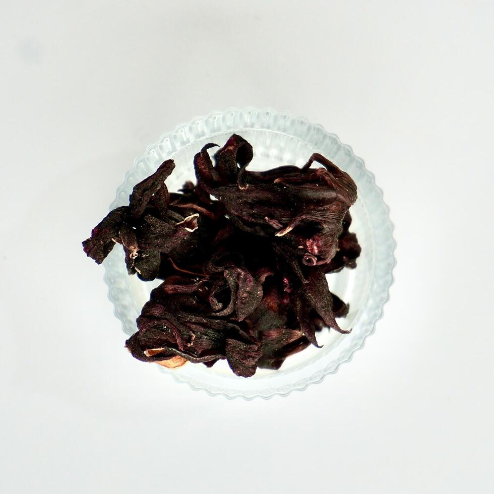 Dry purple rosella hibiscus flower herb tea in round glass bowl isolated on square white background from above angle view. photo