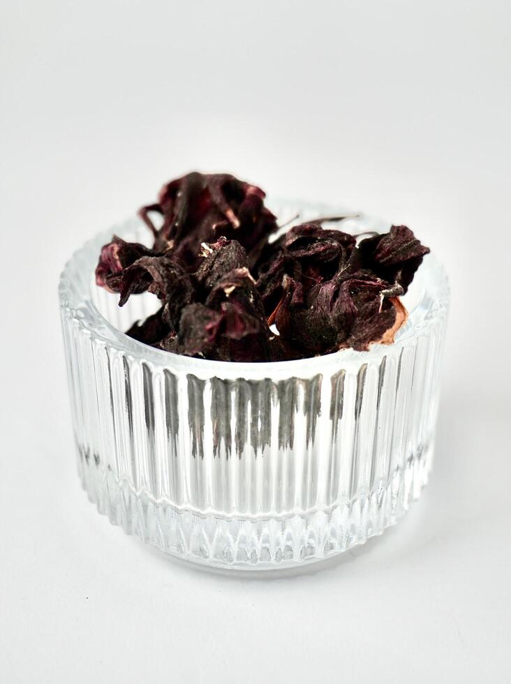 Dry purple rosella hibiscus flower herb tea in round glass bowl isolated on vertical white background. photo