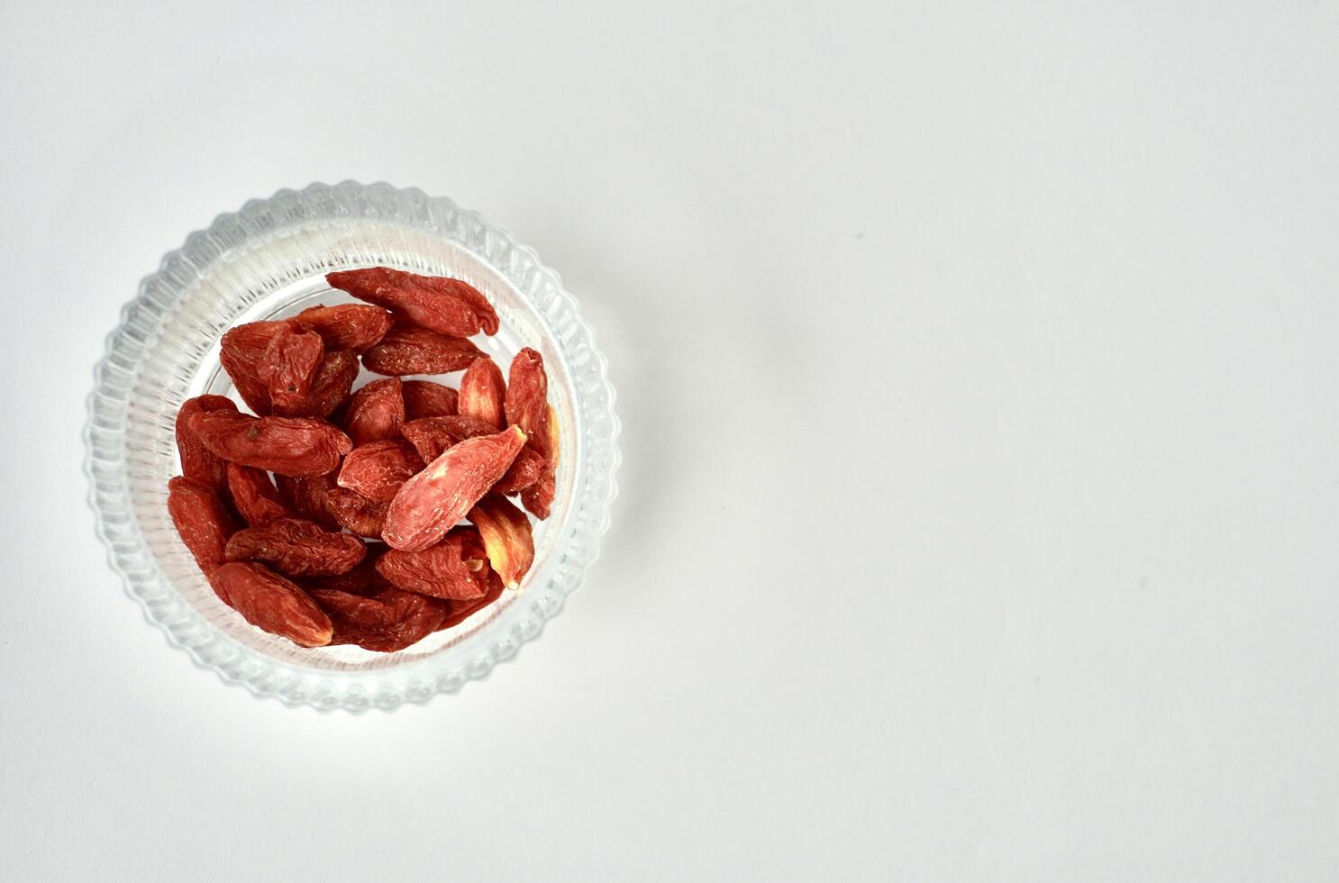 Dry red goji berry food and drink ingredients in round glass bowl isolated on horizontal copy spaced white background. photo