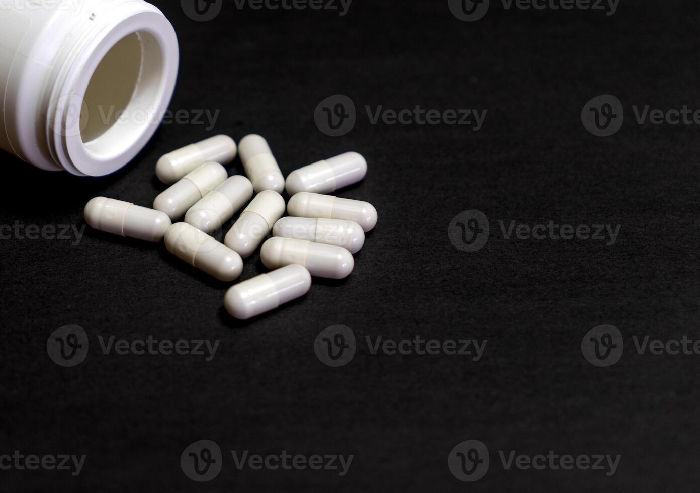 Pills spilled out of white bottle on black background. Mock up for special offers as advertising or other ideas. Medical, pharmacy and healthcare concept. Copy space. Empty place for text or logo. photo