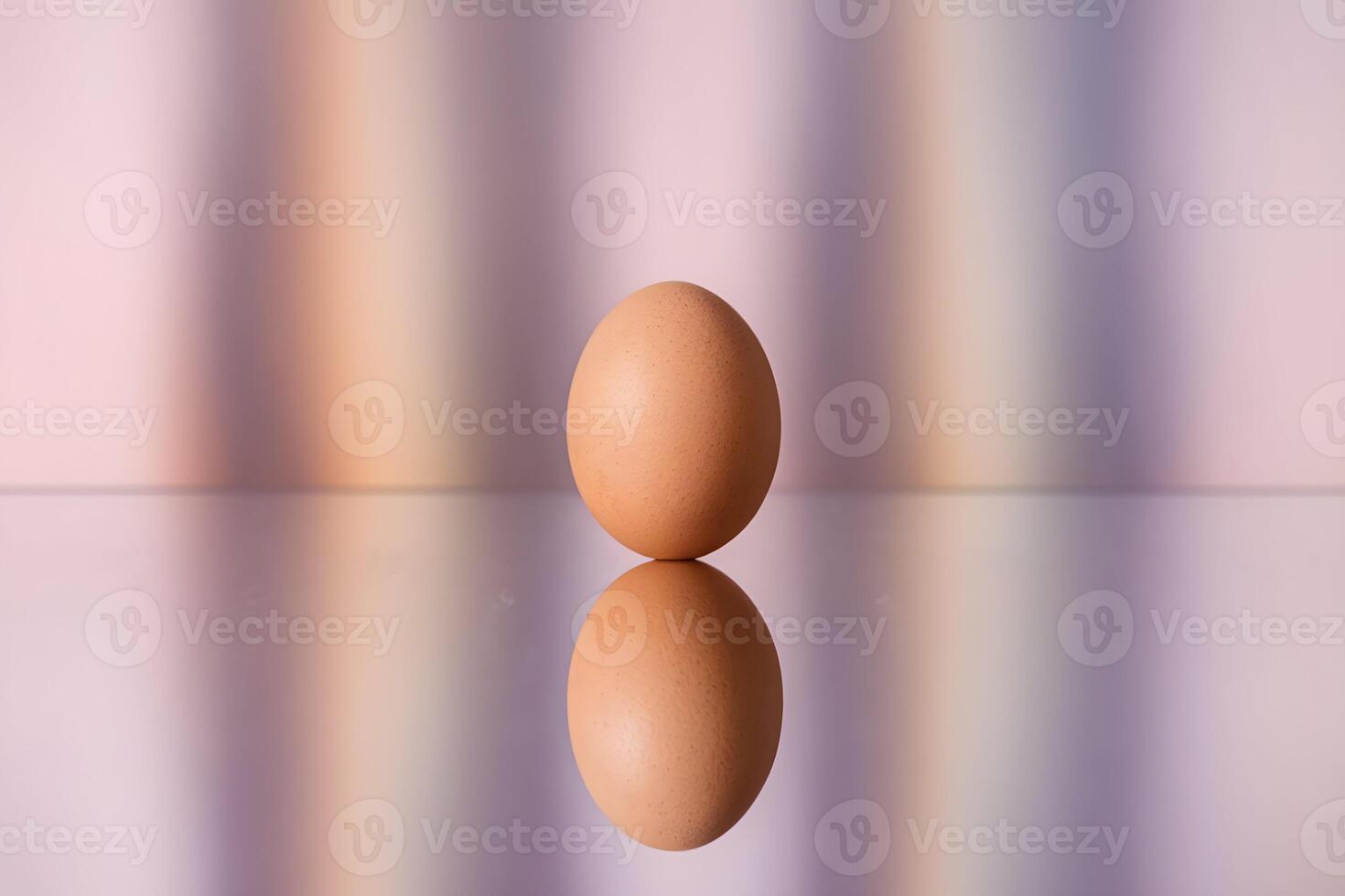 A single egg stands upright, reflected on a surface against pastel hues photo