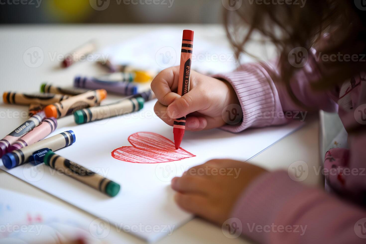 Child draws red heart with crayon, surrounded by vibrant scattered crayons photo