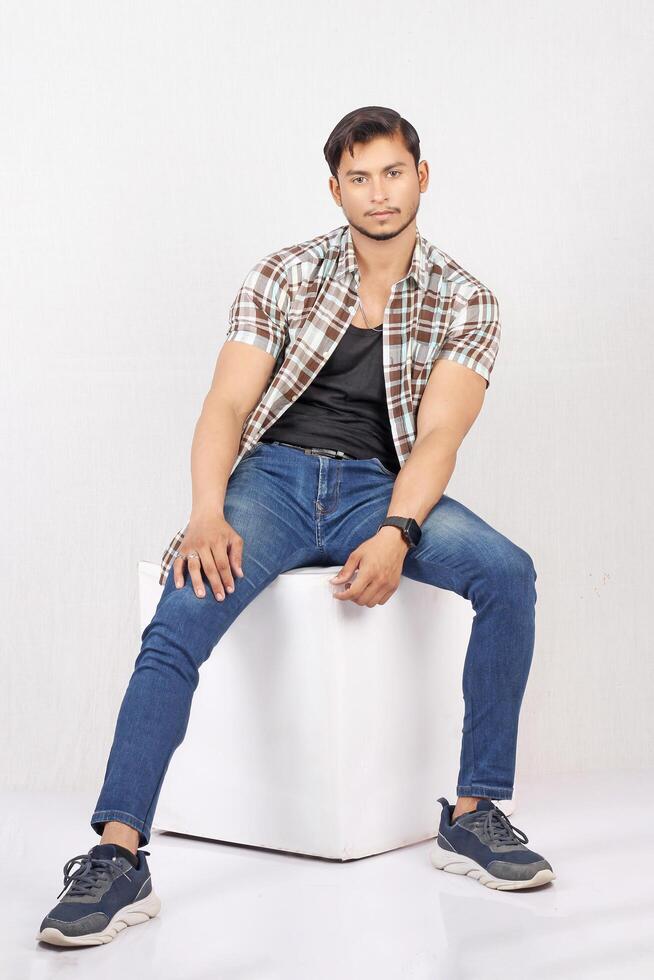A man in jeans and shirt sitting on a white box photo