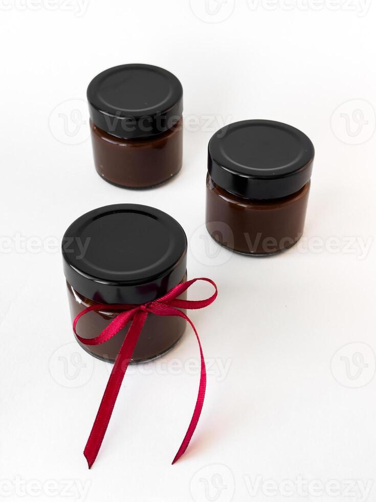 Three chocolate spread jars on white background with red ribbon accent photo