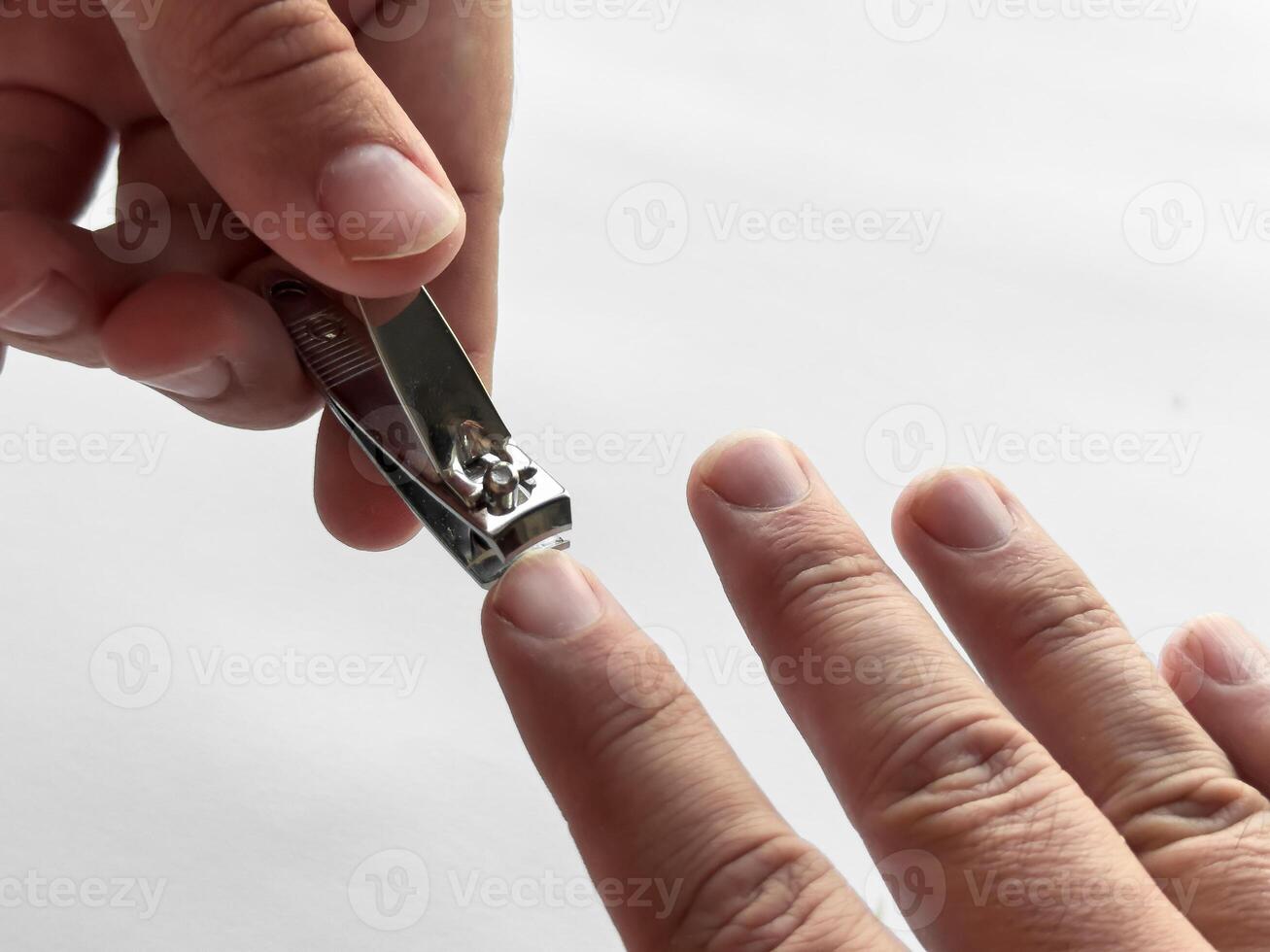 Close up of hand using nail clipper for personal grooming on white background photo