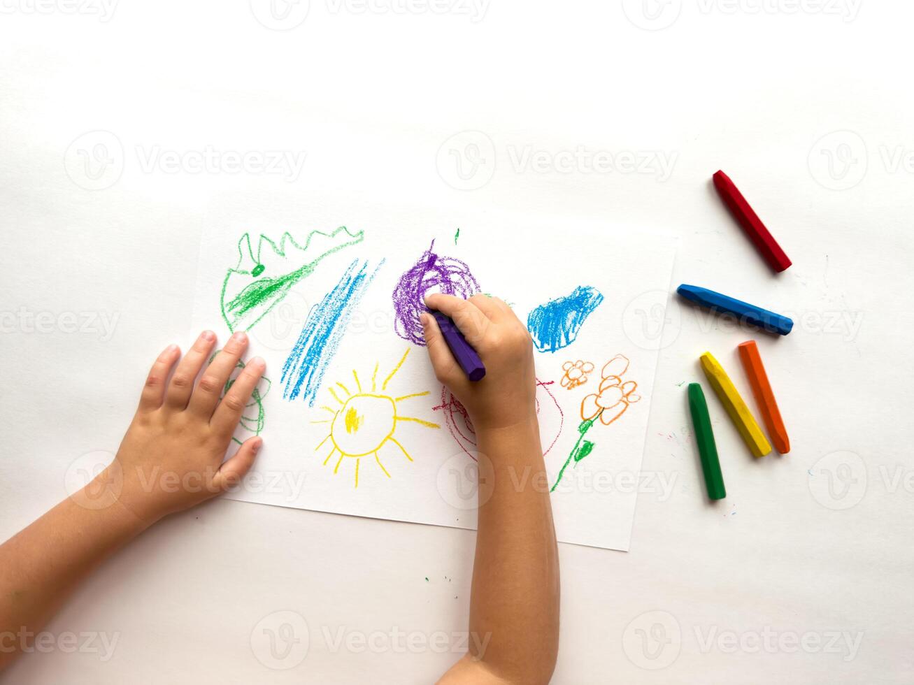 Child drawing with colorful crayons on white paper photo