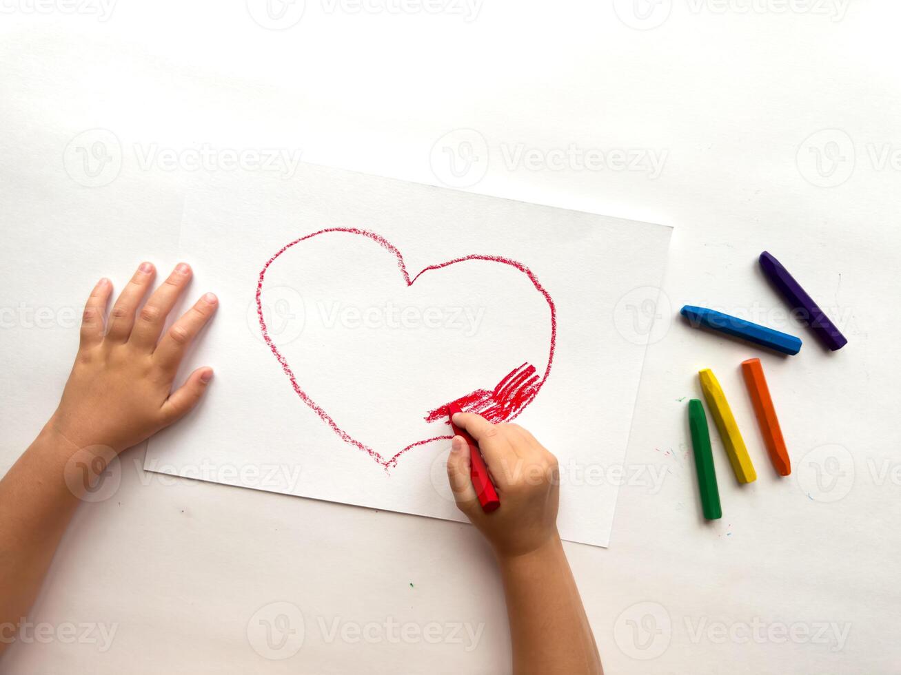 Child drawing heart with crayons on white paper. Creativity and expression photo
