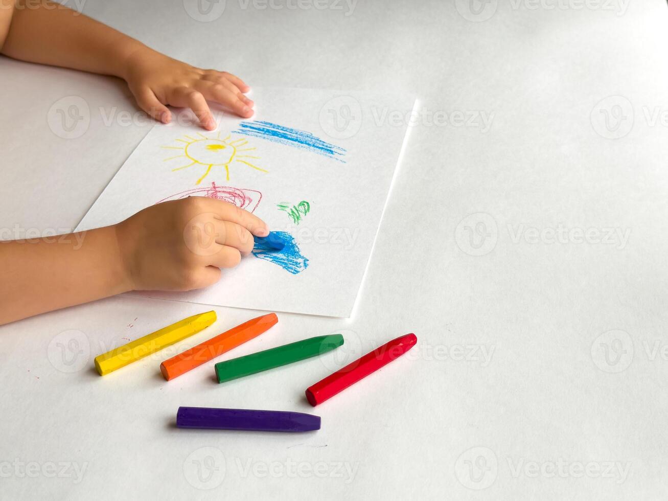 Child drawing with crayons on white paper creates colorful artwork photo