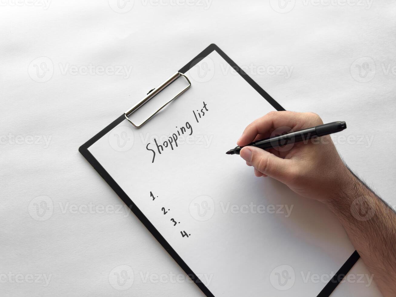 Hand writing shopping list on clipboard with pen on white background photo