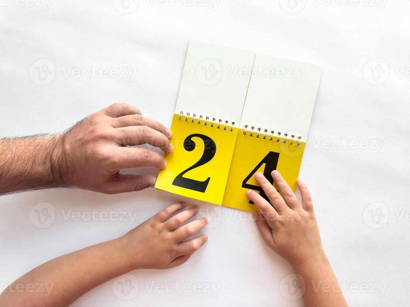 Parent and child turning pages on yellow calendar against a white background photo