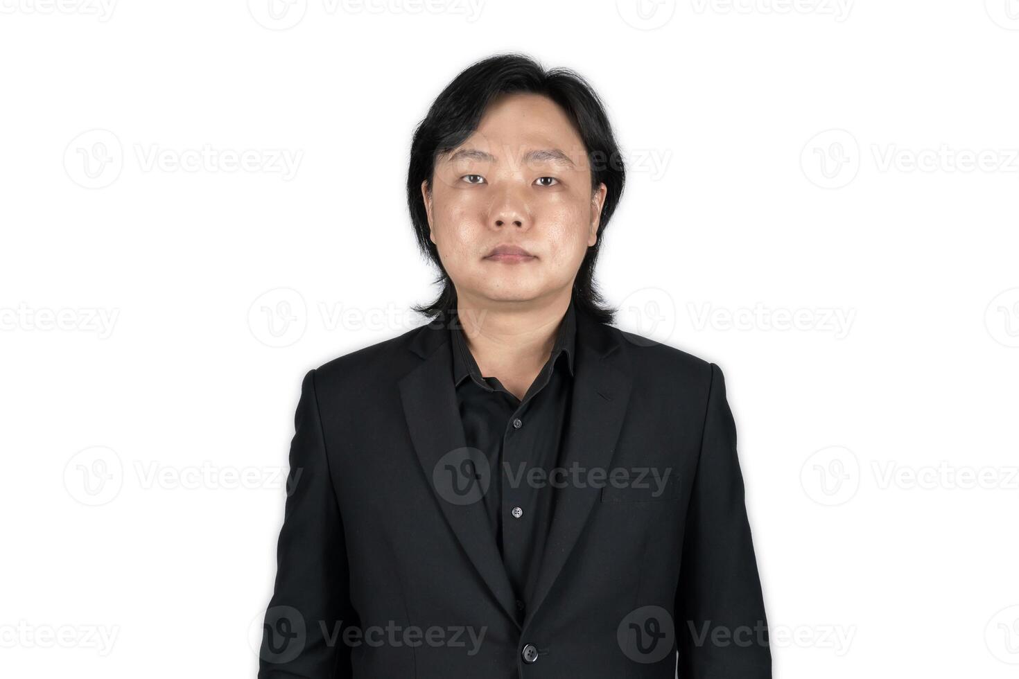 The portrait of a young Asian man wearing the tidy black suit with plain expression on the white grey background shot in the studio. photo