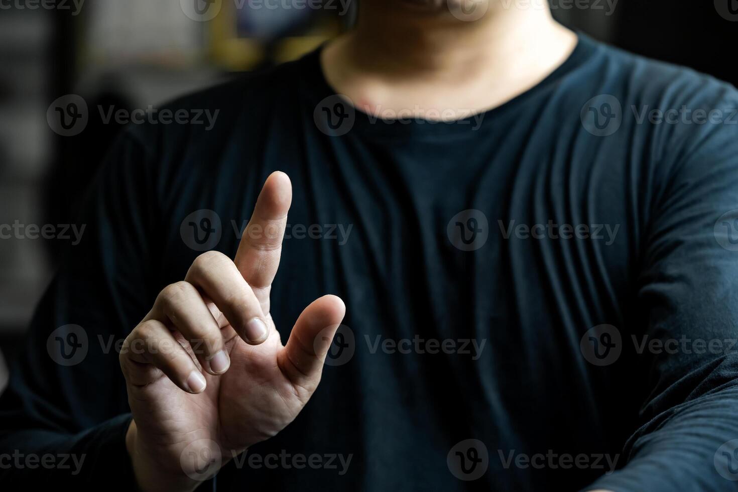 a man in a black long arm t shirt makes hand motions with his thumbs and index fingers in the dark light. photo