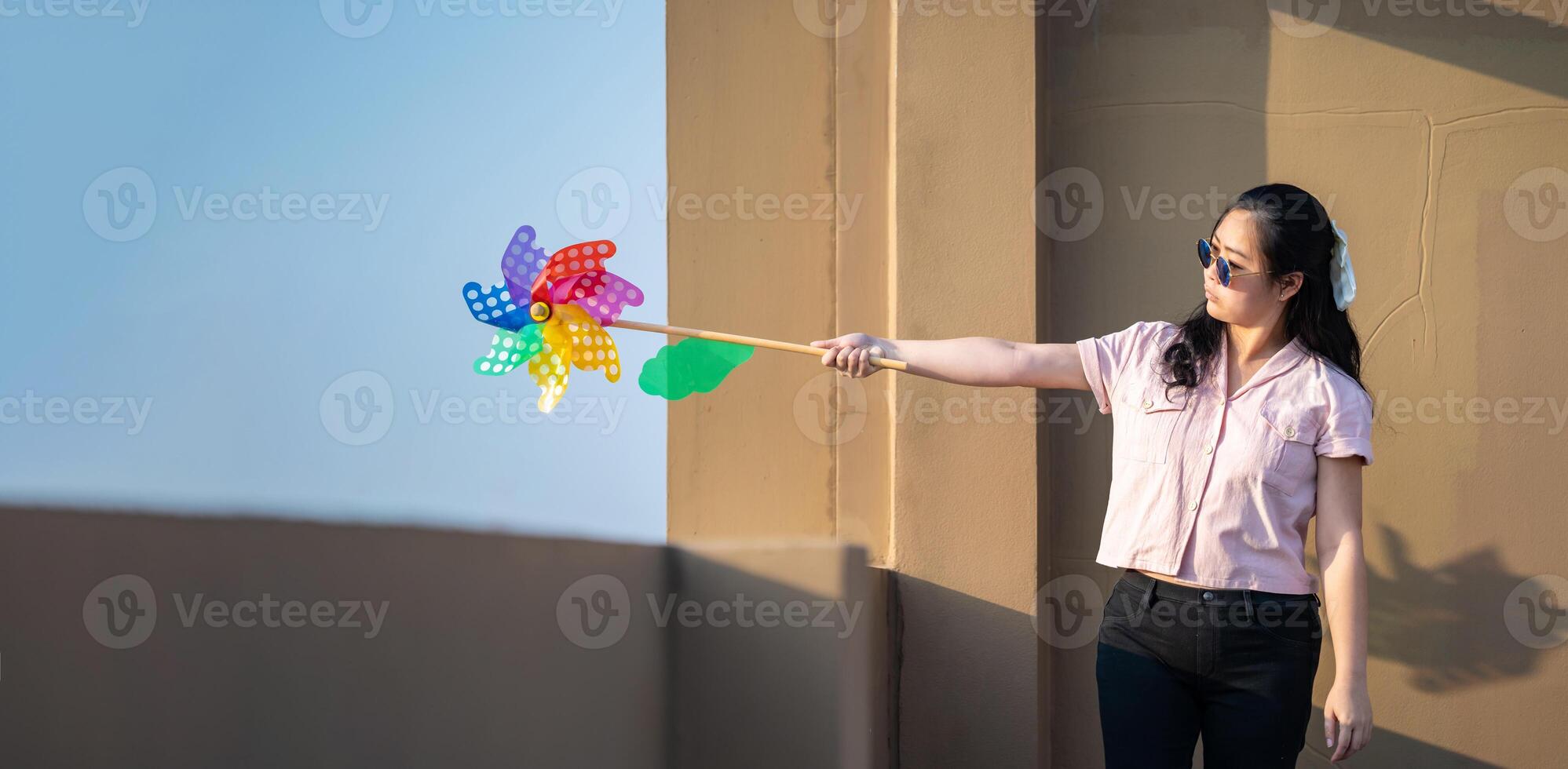 Asian woman posts and play Windmill Toy colourful rainbow colour on the building rooftop in sunset time. photo
