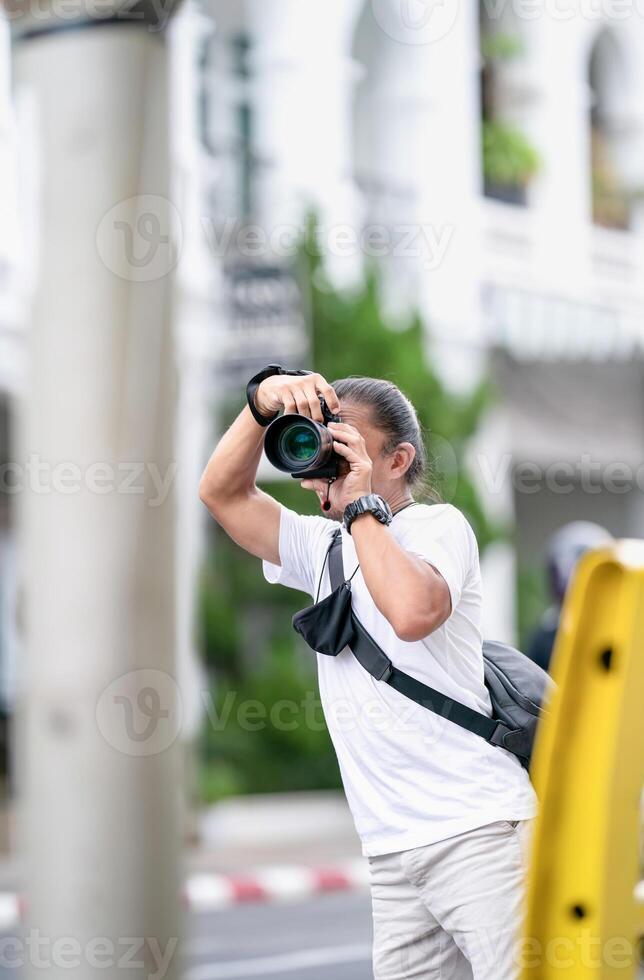 Professional Asian Camera man focus on the image with his mirrorless camera beside the street outdoor field. photo