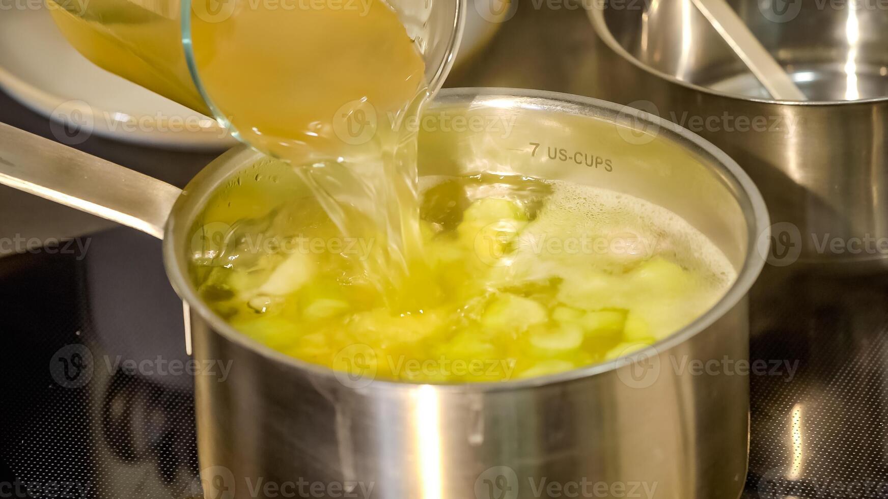 chef expertly adds a splash of water to the sizzling steel cooking pot on the electric stove, causing a burst of steam to rise from the bubbling broth inside. photo