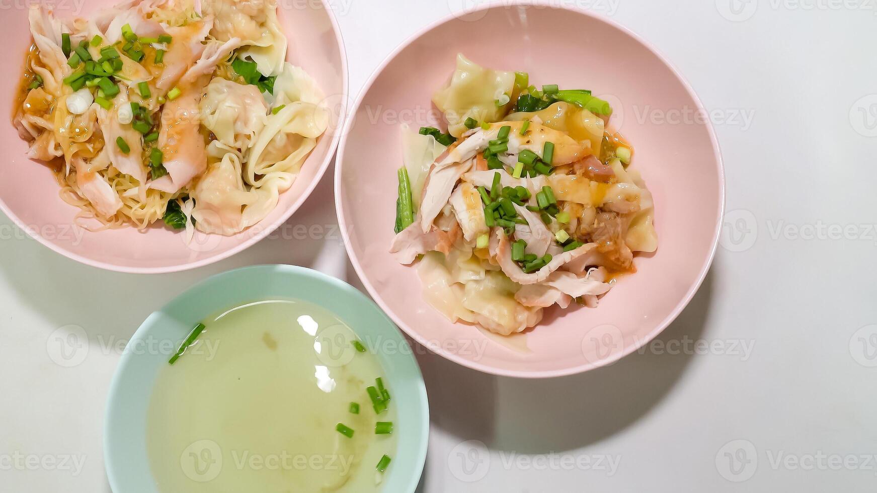 Two bowls of shrimp wonton noodles and a bowl of soup were placed on the table. photo