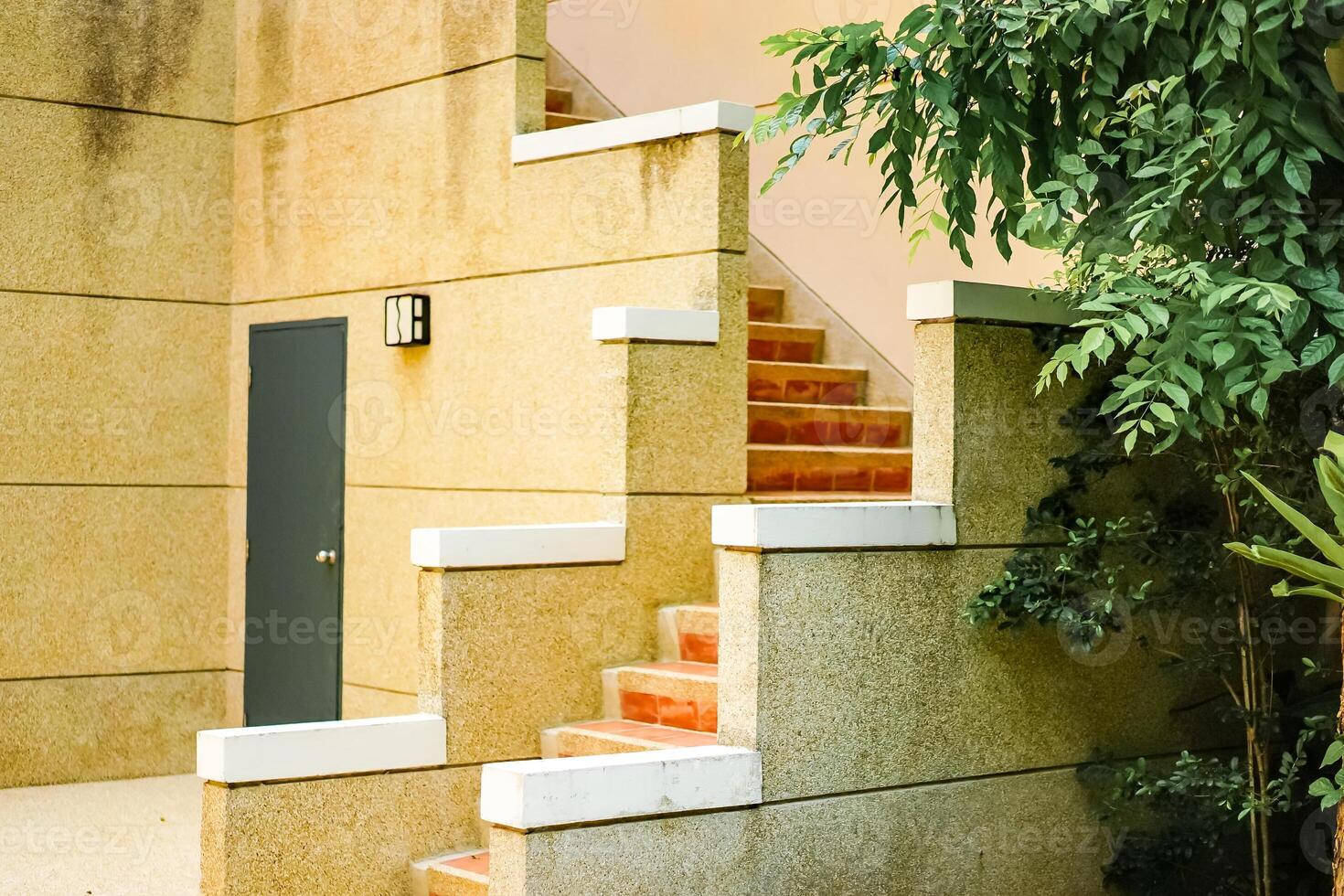 The exterior stone stairway with masonry floor and stone handrail at the courtyard of the classic modern style resort to the second floor of the building. The green door on the stone wall. photo