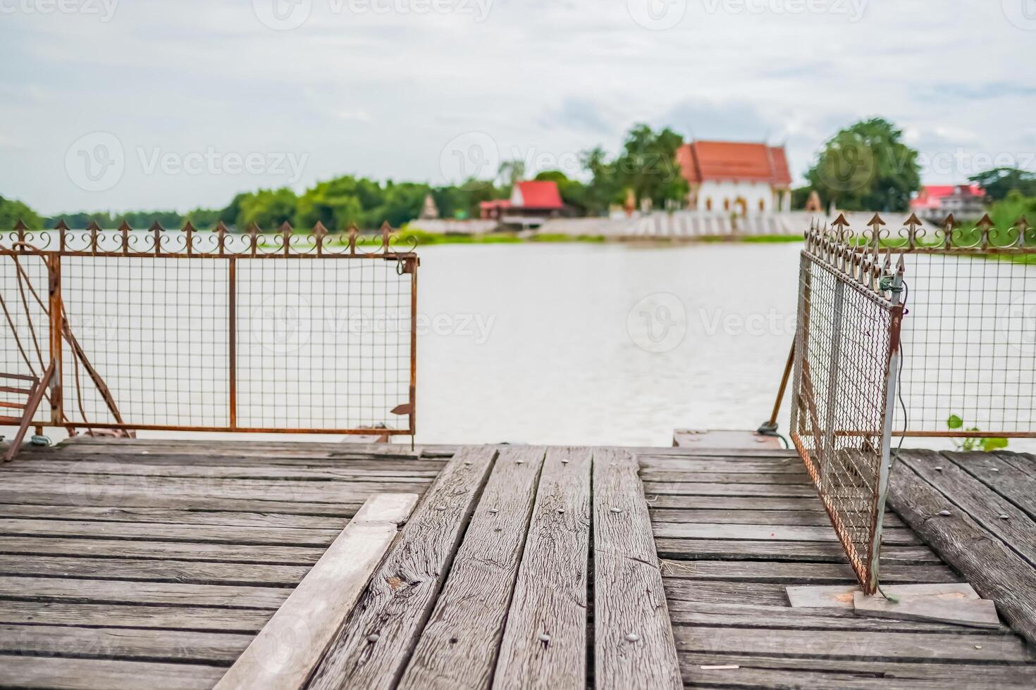 The old wooden dock with decayed iron fences beside a river in Thailand. A temple at the serene riverside. photo