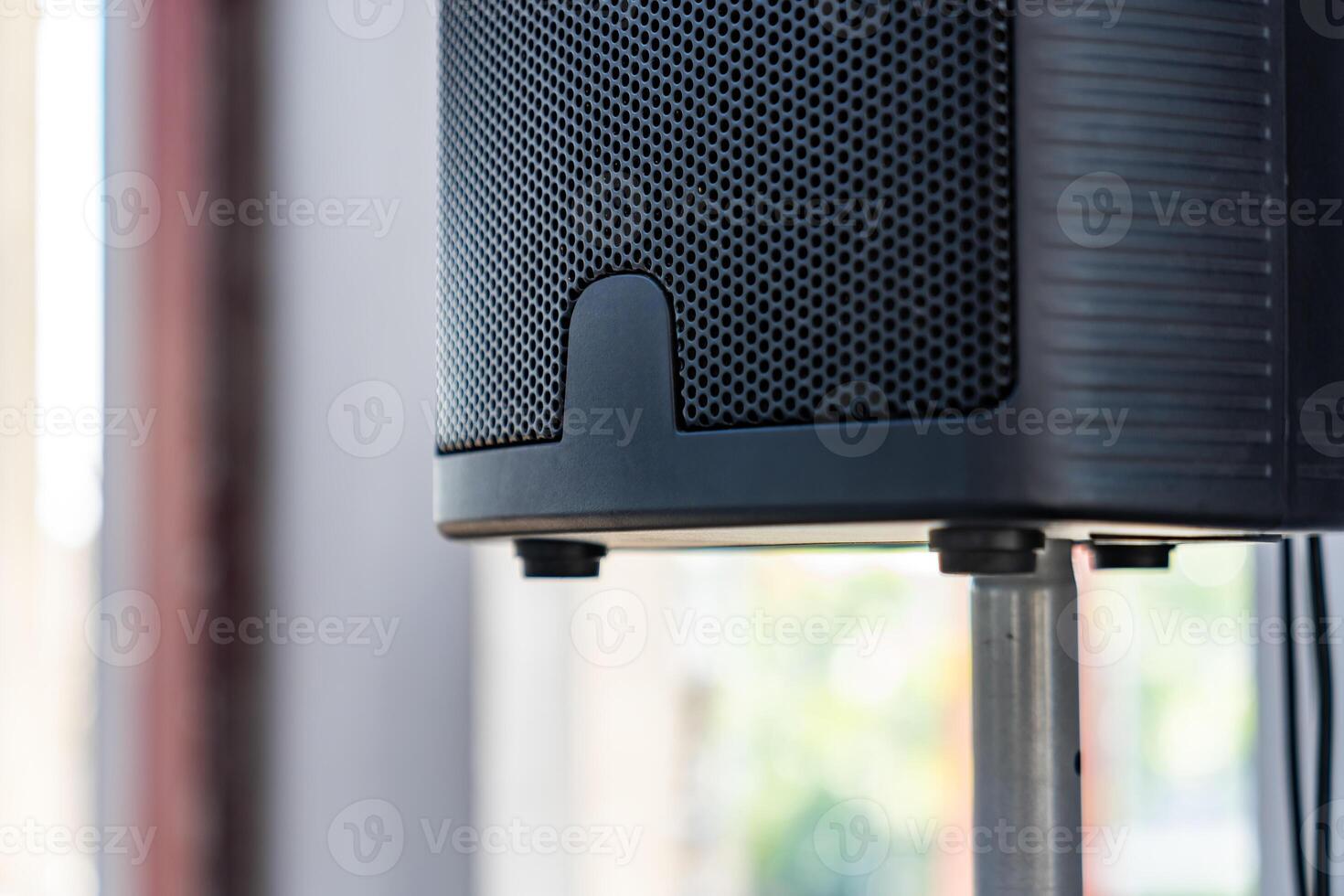 The close up photo of the modern black speaker and the metallic stand on a blurry background.