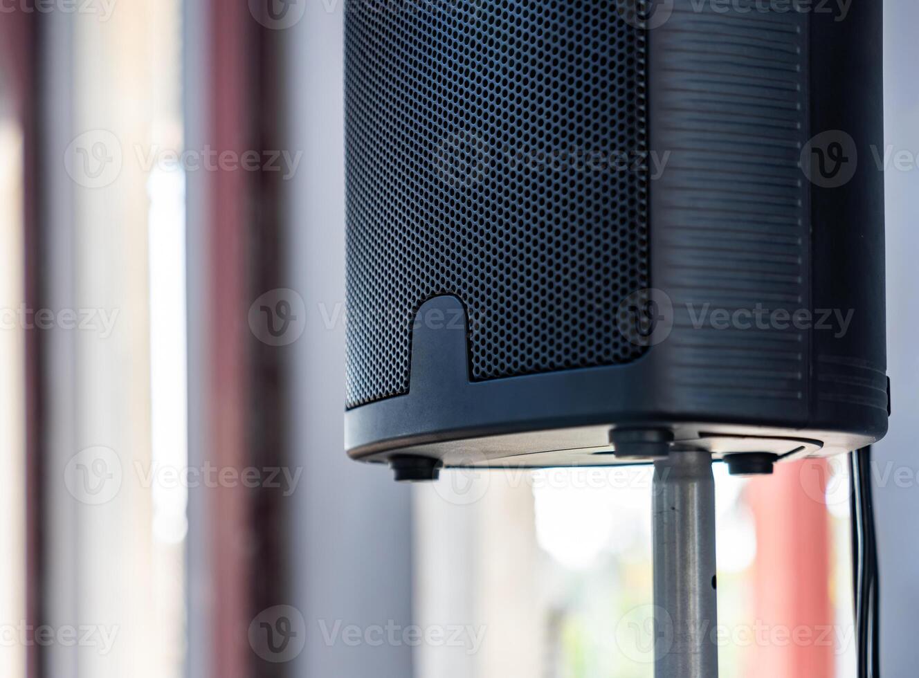 The close up photo of the modern black speaker and the metallic stand on a blurry background.